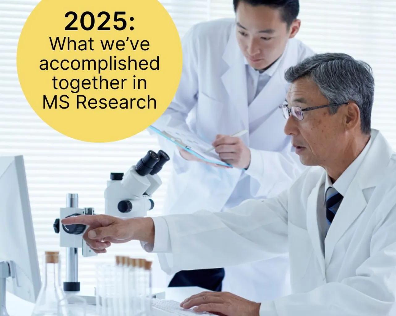 Two researchers in white lab coats. One pointing to a computer screen and one holding a clip board.