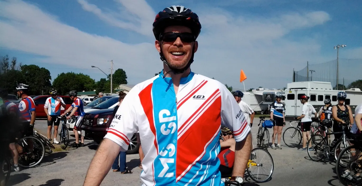 Craig wearing an MS Bike jersey standing in front of his bike outside.