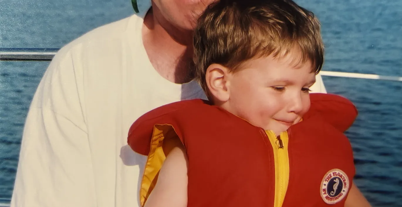 Larry in sunglasses holding his son Glen in a red life jacket on a boat.