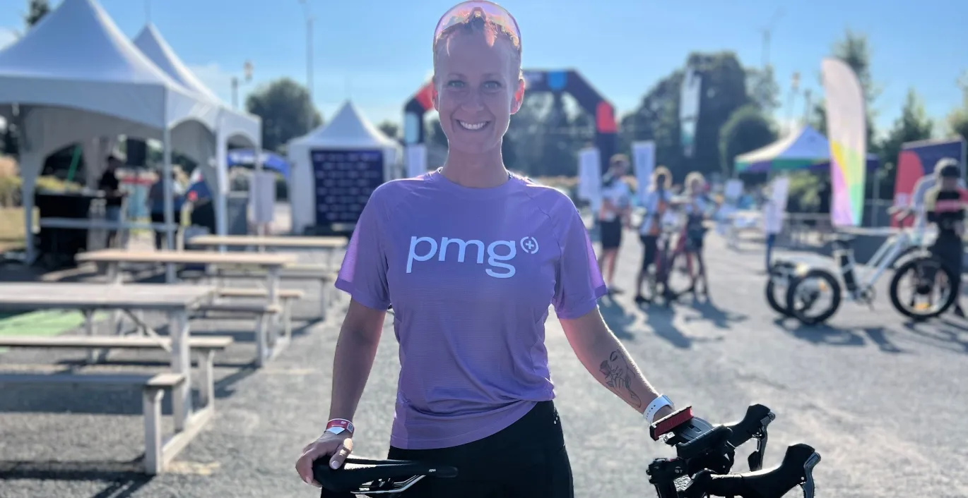 Chantal standing with a road bike at an outdoor event, wearing a purple PMG shirt.