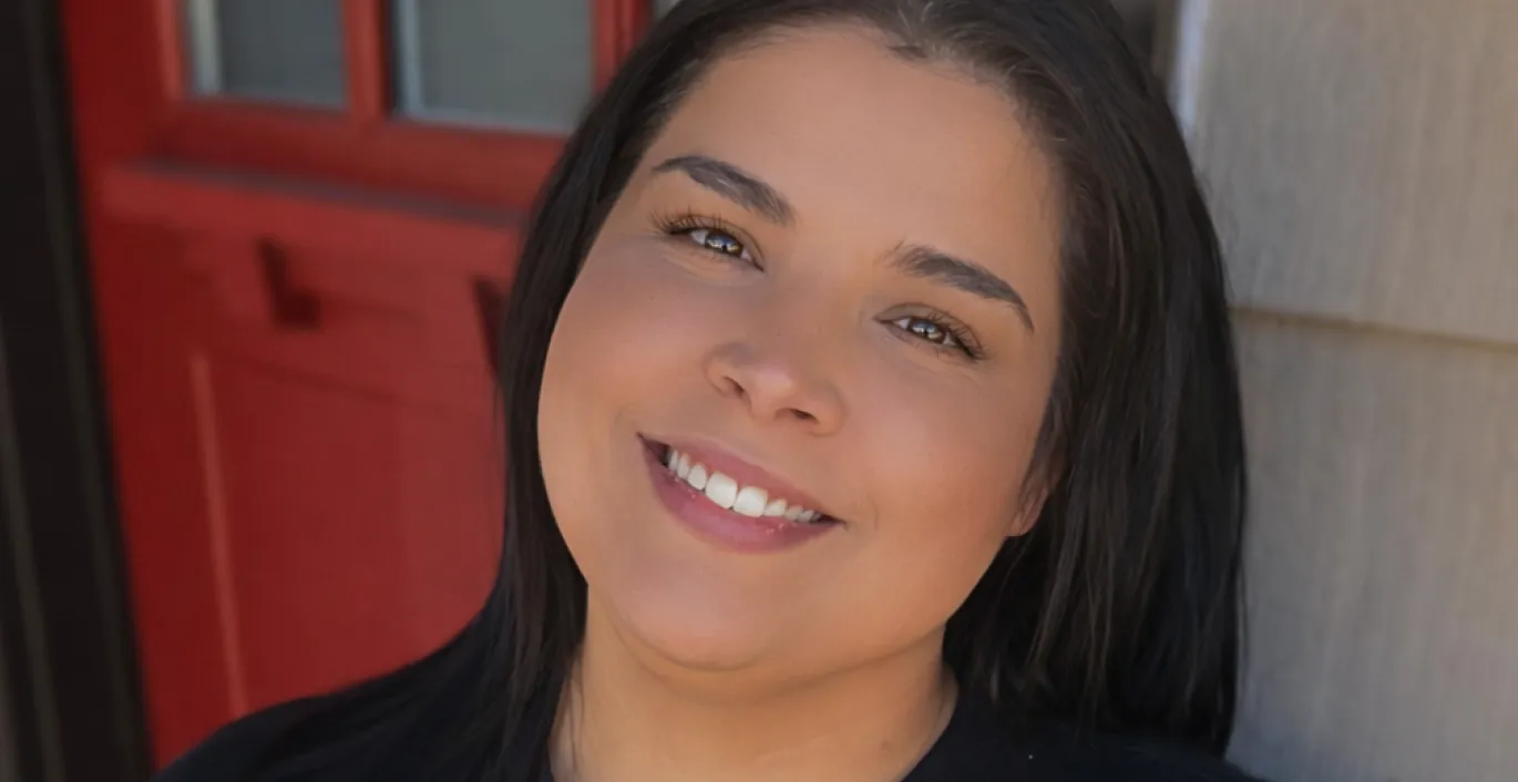 Rachel smiling in a black "quietly powerful" sweatshirt, standing near a red door.