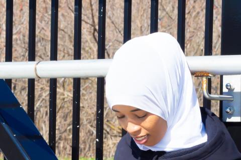 Najma sitting and looking down while pointing at black hoodie that reads 'Multiple Sclerosis Warrior.'