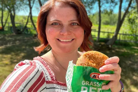 Caitlin smiling and holding a Teen Burger® outside with trees in the background