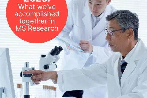 Two researchers in white lab coats. One wearing glasses and pointing at a computer screen and one holding a clipboard and pen.