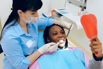 A dentist examining a patient who is looking in a small handheld mirror.