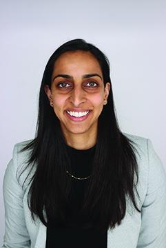 A woman with long dark hair is wearing a light green cardigan and black shirt. She is smiling.
