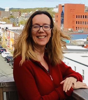 A woman with light brown hair and glasses smiles.