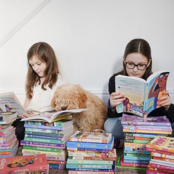 Beatrice and Emmeline sitting on the floor while reading books with their dog.