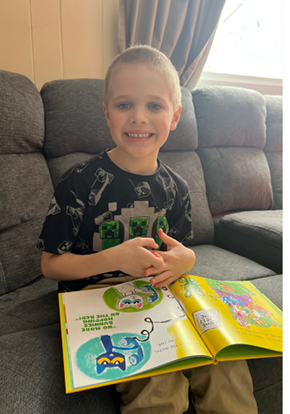 Jaxin, sitting on a couch, wearing a black shirt, with a book on his lap.