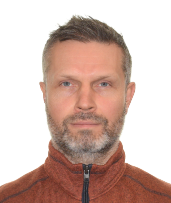 A man with very short brown hair and a short beard is wearing an orange zip up sweater.