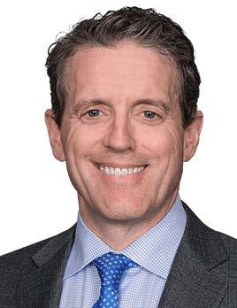 A man with short, dark hair is wearing a grey suit and blue tie.