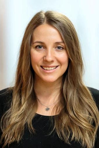 A woman with long, wavy dark blonde hair is smiling.