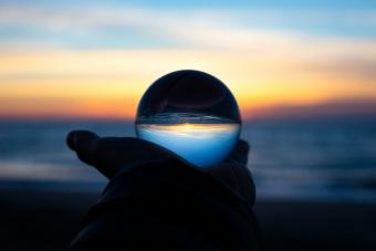 Hand holding a crystal ball reflecting a vivid sunset over the ocean.