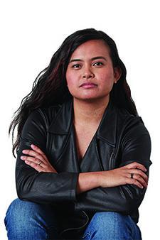 Woman in black leather jacket sitting with arms crossed, looking serious.