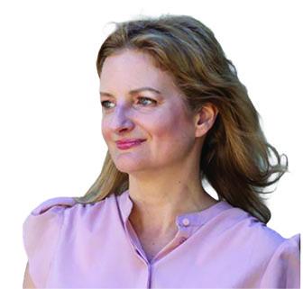 Woman with brown hair smiling softly, wearing a light pink blouse, photographed outdoors.