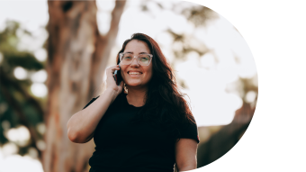 Woman smiling while talking on phone outdoors, with trees in the background.