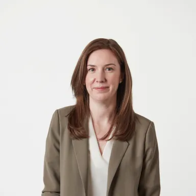 Professional headshot of a smiling woman with brown hair wearing a tan blazer.