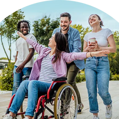 Four diverse, joyful friends outdoors, one using a wheelchair, laughing together on a sunny day.