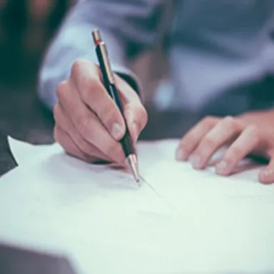 Person signing or writing on a document with a pen, close-up view.