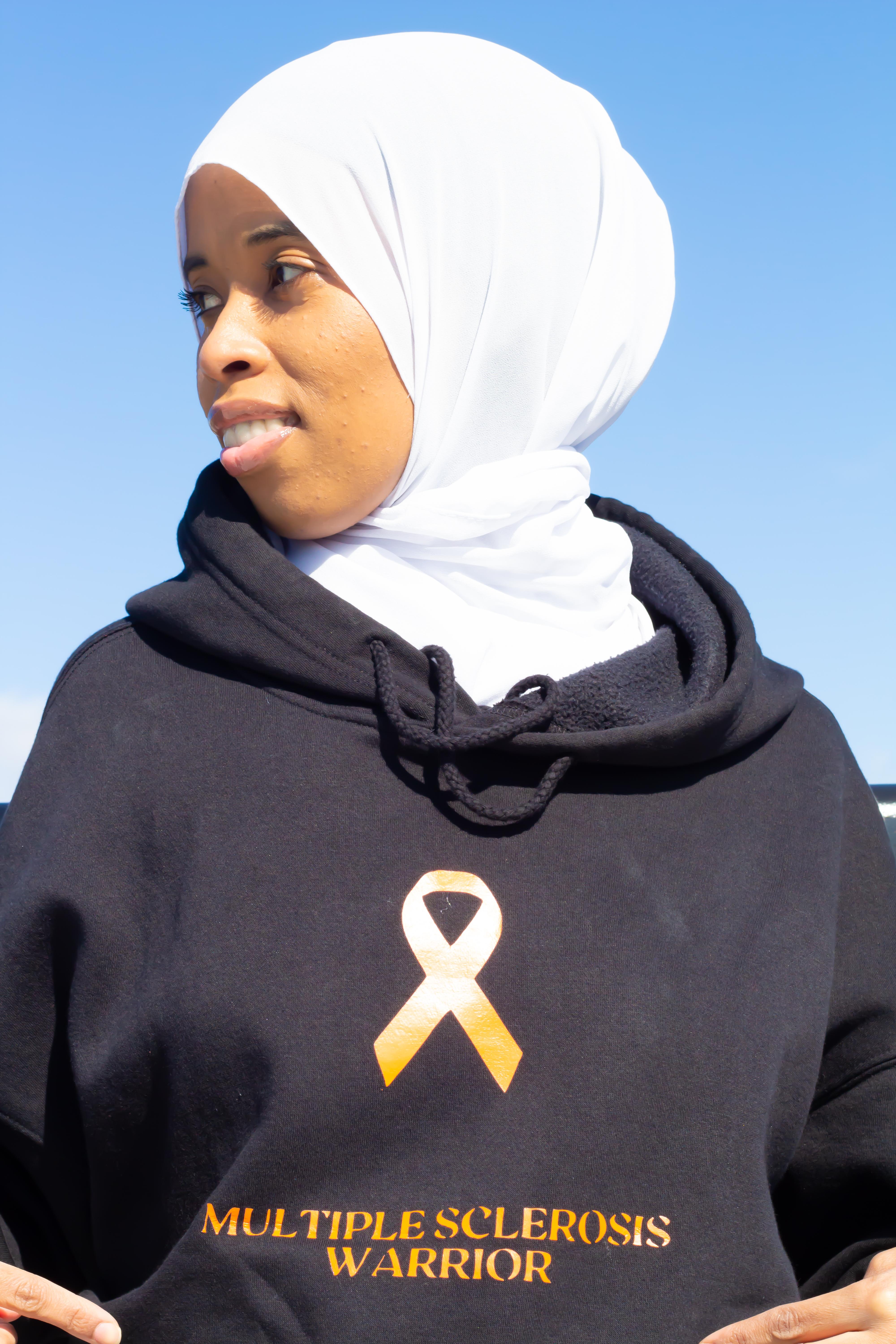 Najma looking off to the side while wearing black hoodie that reads 'Multiple Sclerosis Warrior.’