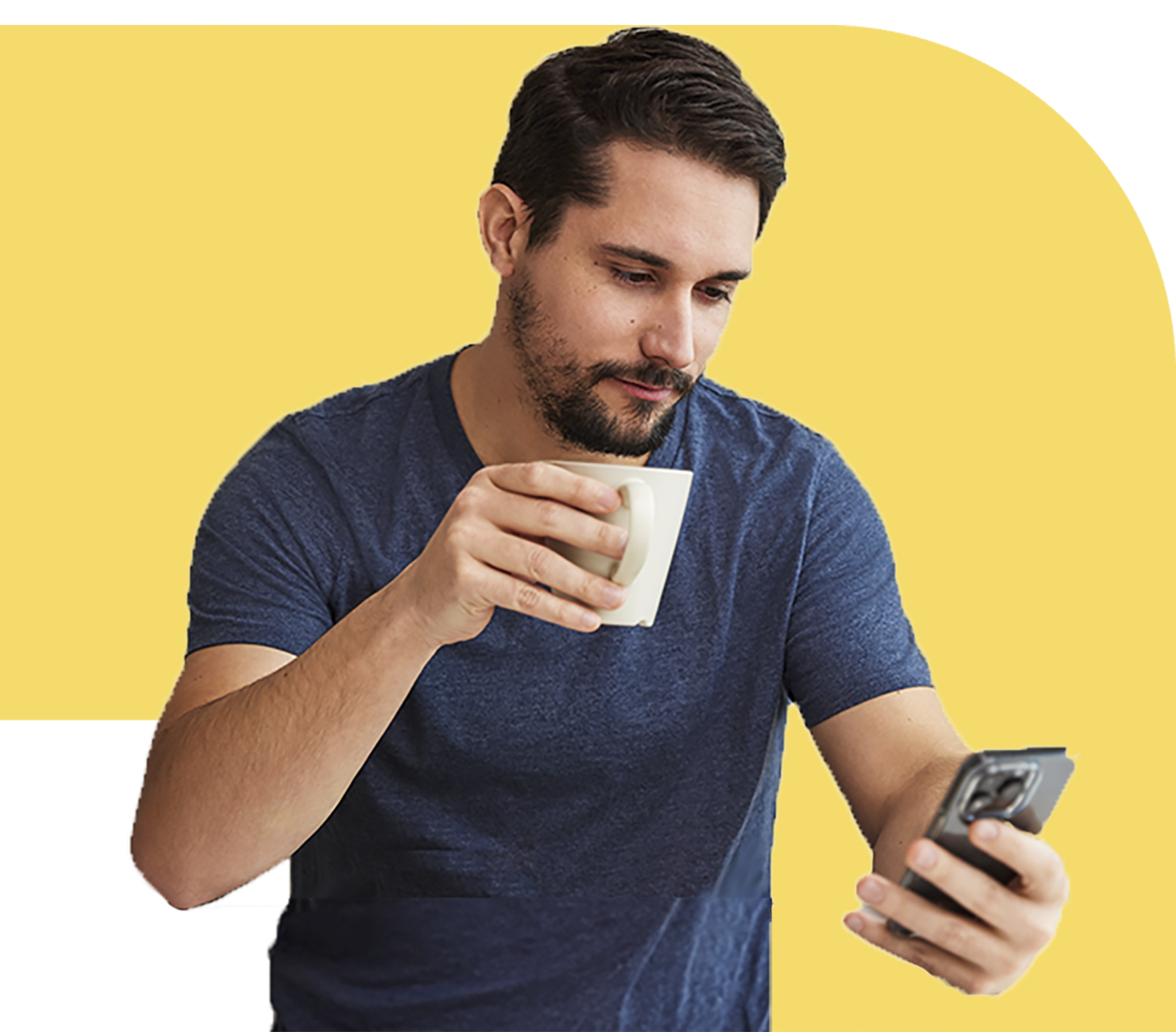 A man with short dark hair and a goatee wearing a dark blue t-shirt sips coffee and reads his phone intently.