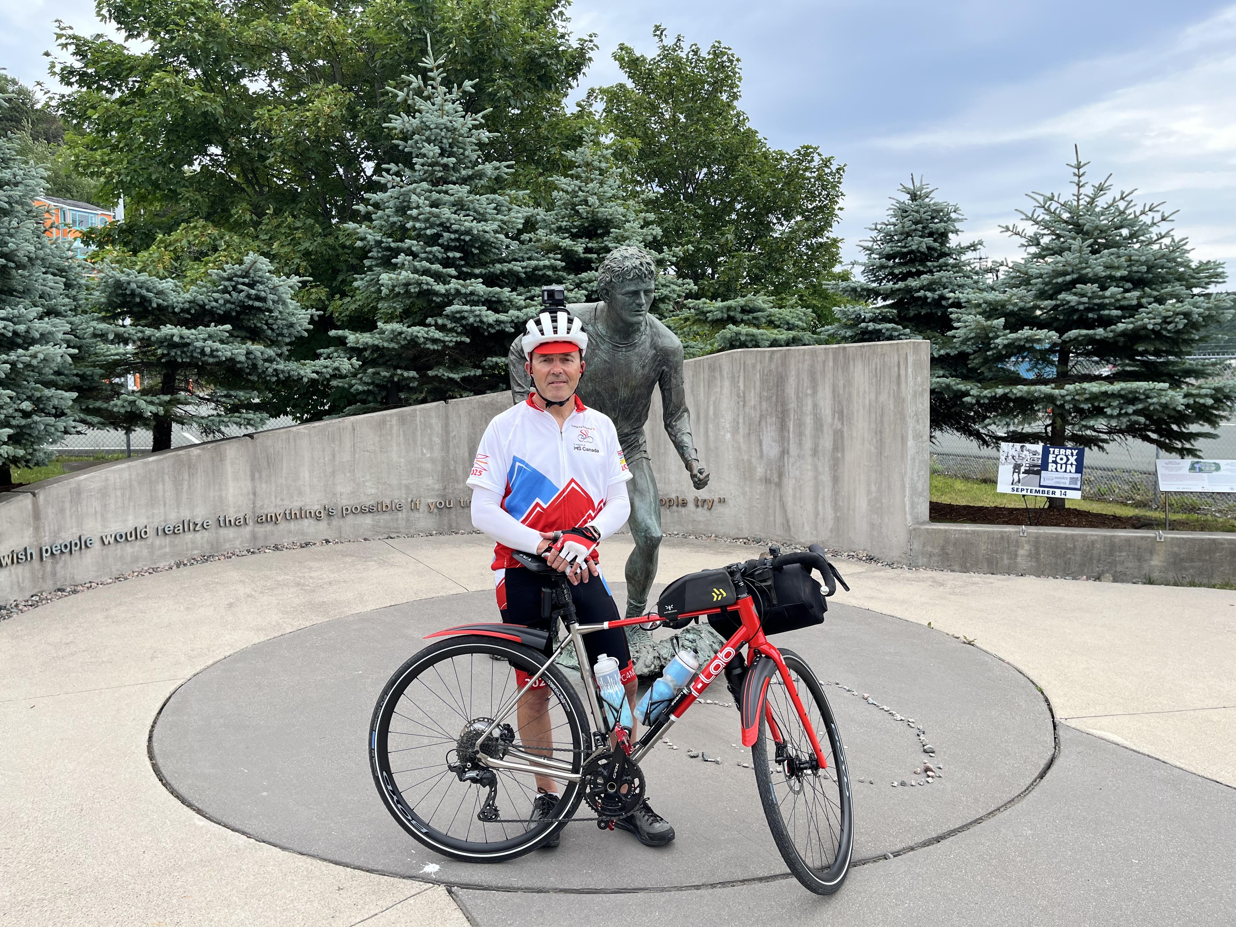 Marcel standing with his bike in front of a Terry Fox monument in St. John's, Newfoundland.