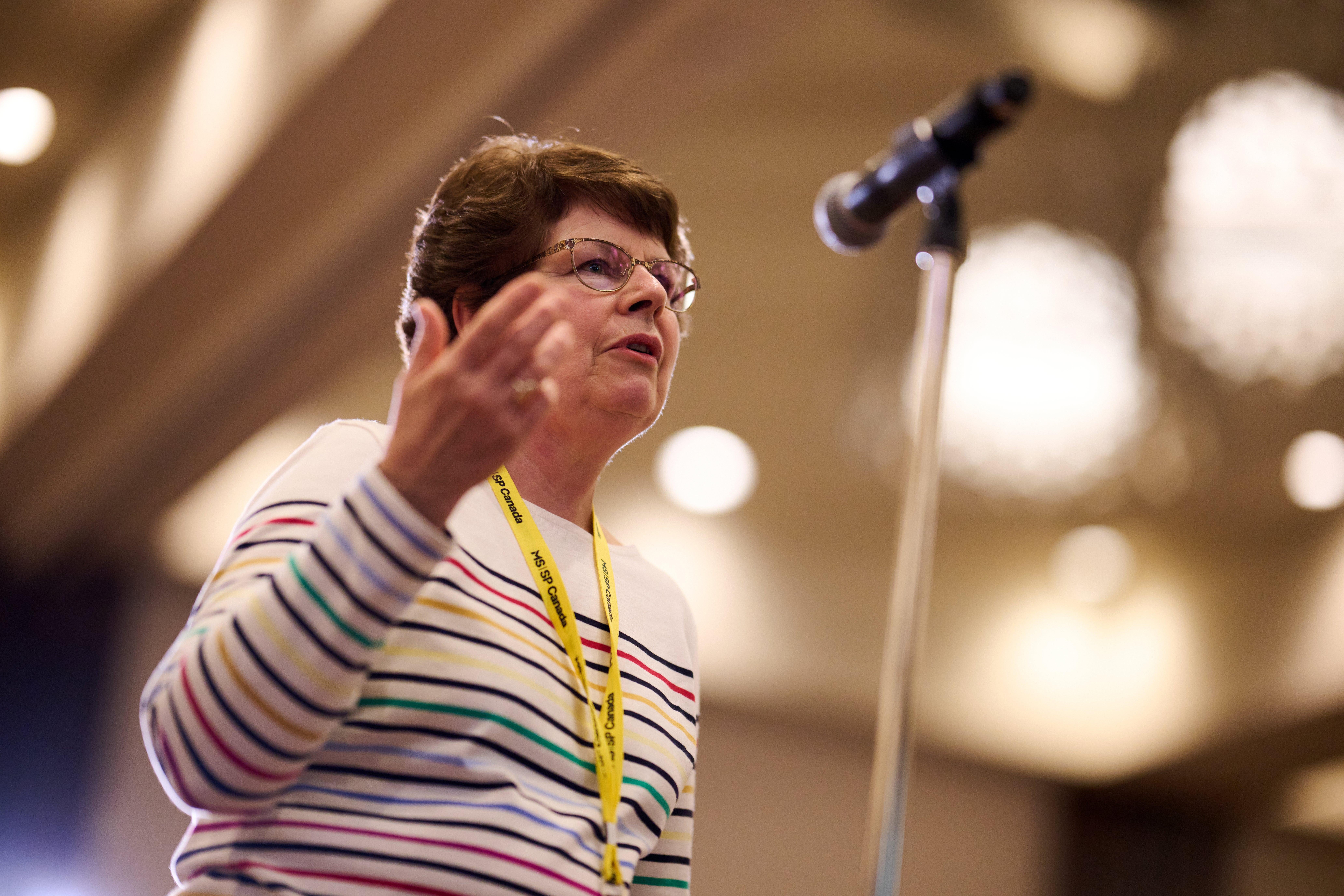 A woman with short brown hair and glasses is speaking in to a microphone.