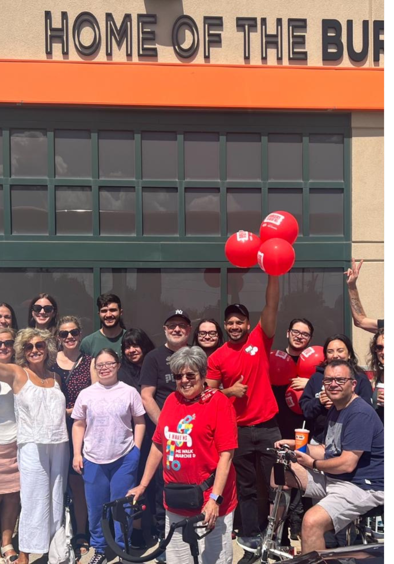 Vivek holding Burgers to Beat MS balloons, standing outside his A&W location with staff and community members