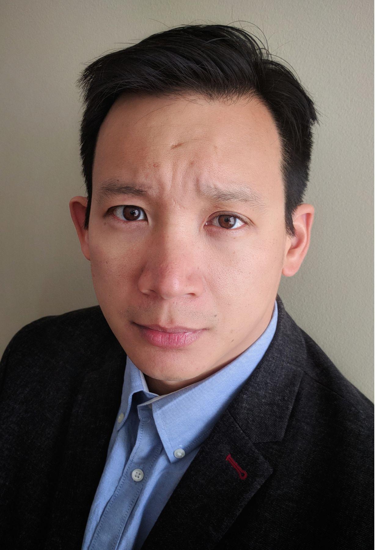 A headshot of Dr. Chan wearing a blue collared shirt and black coat