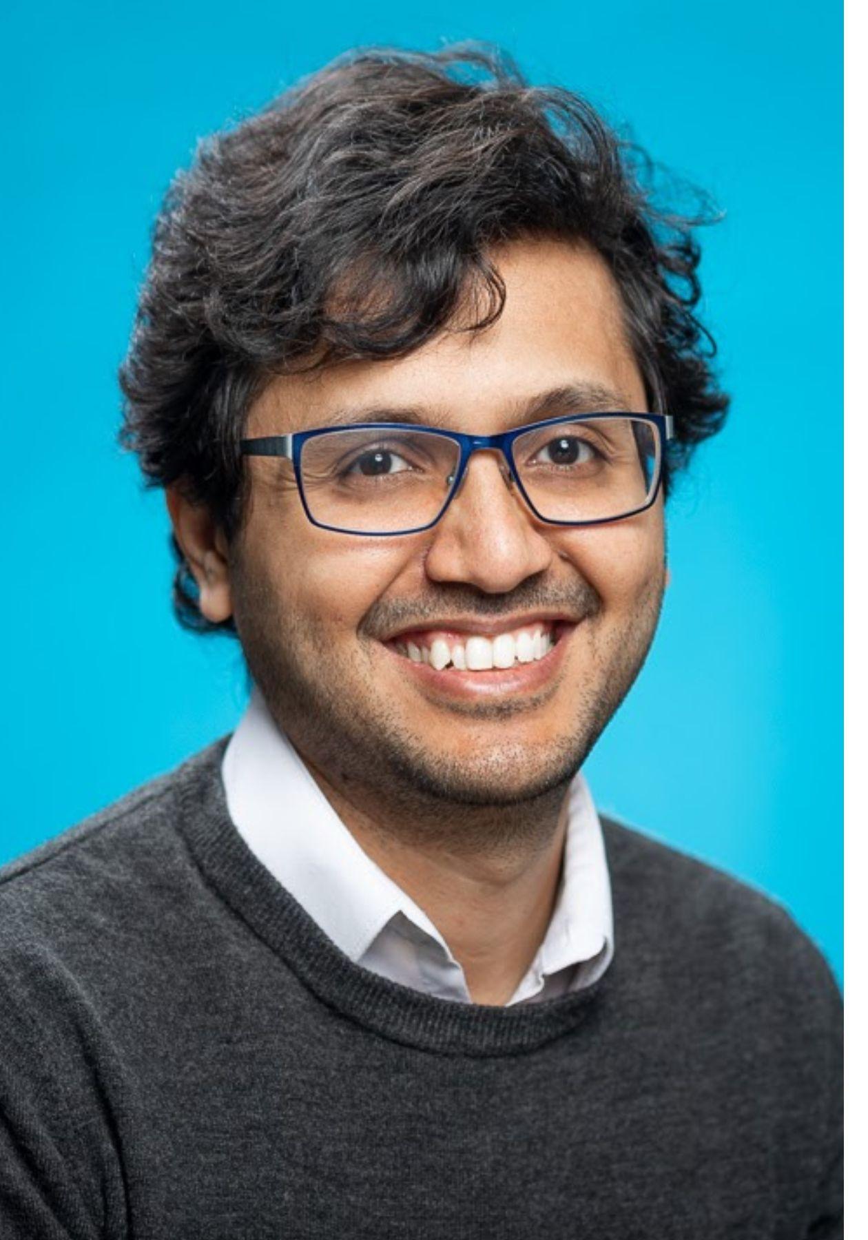 Dr. Manav Vyas smiling in a headshot with a blue background