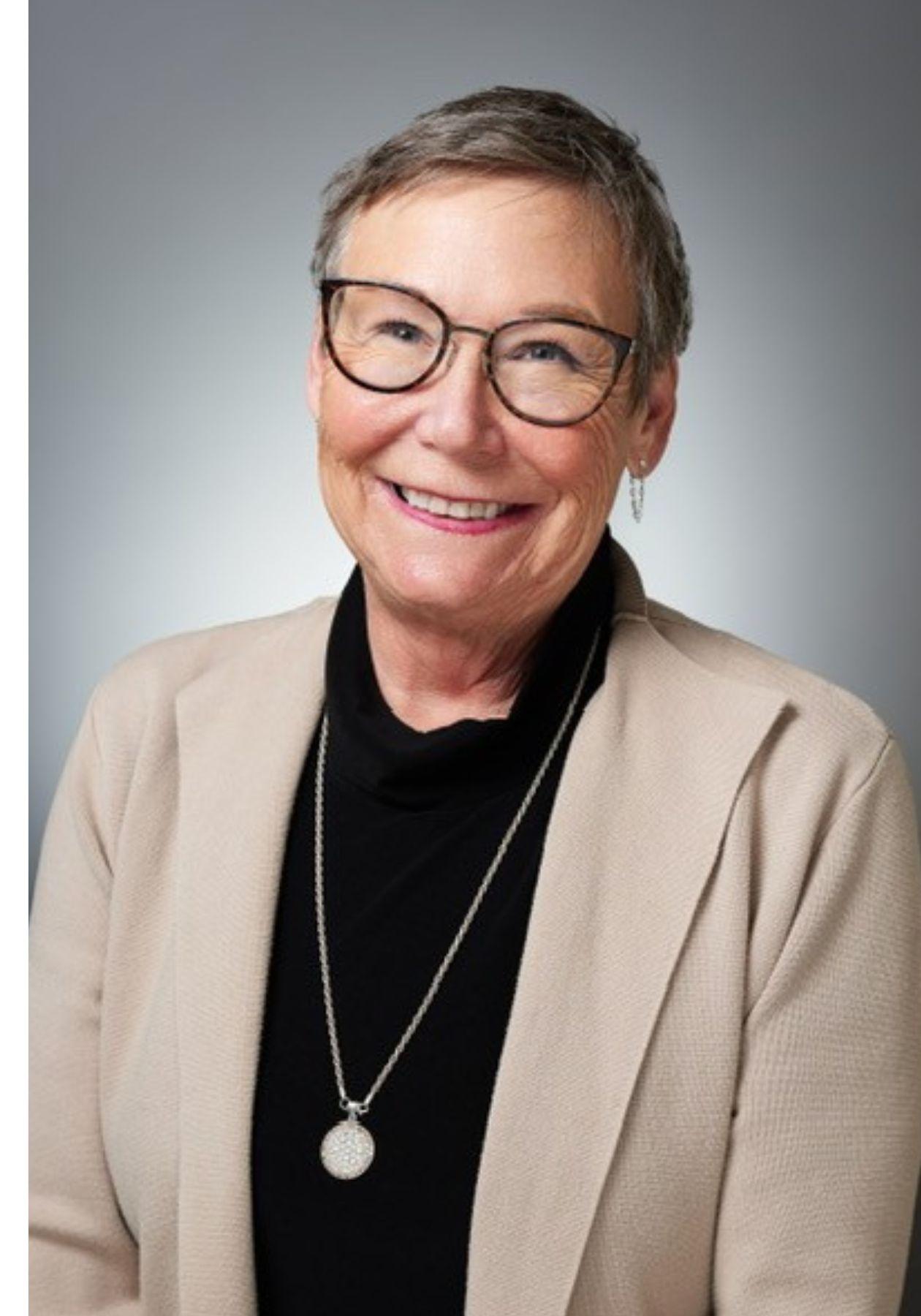 Diana smiling, wearing glasses, black shirt, cream blazer, and necklace