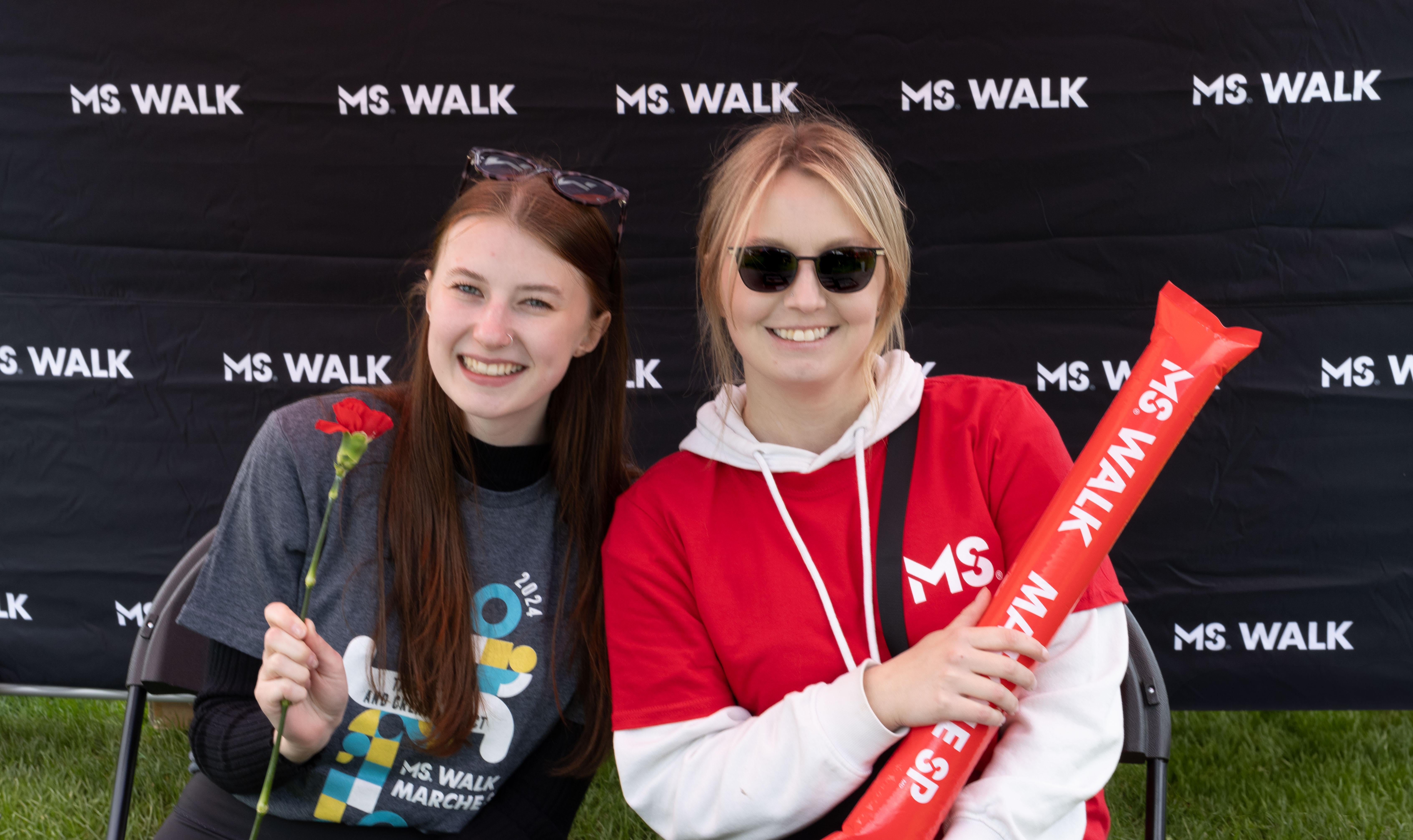 Paige and another woman, holding a red inflatable stick at an MS Walk event.