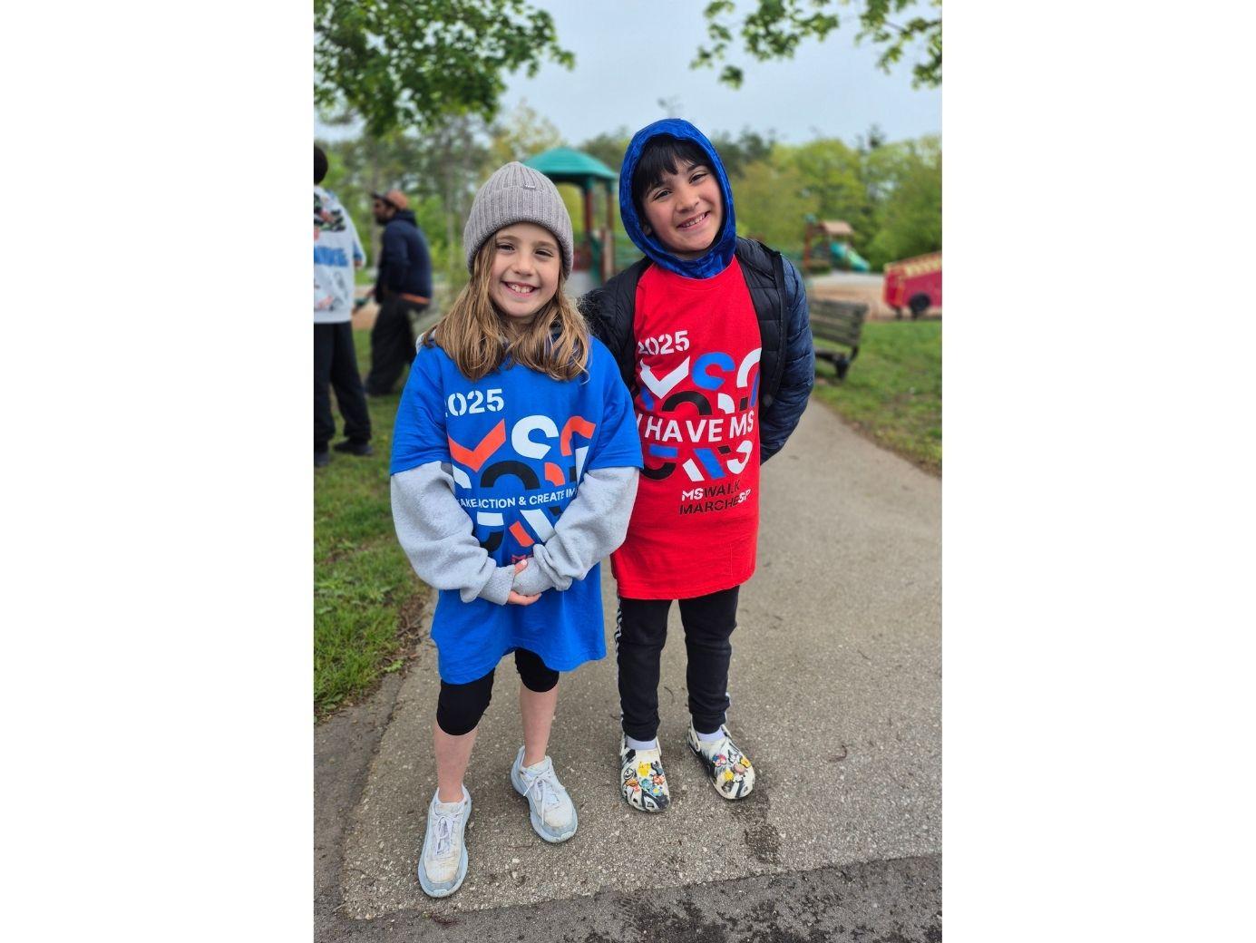 Two young children in colorful hoodies smiling outdoors at a charity run event.