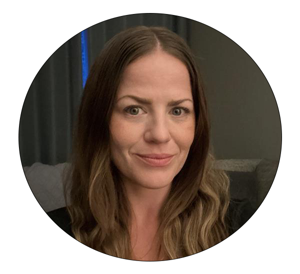 Smiling woman with long brown hair wearing a black top, seated indoors.