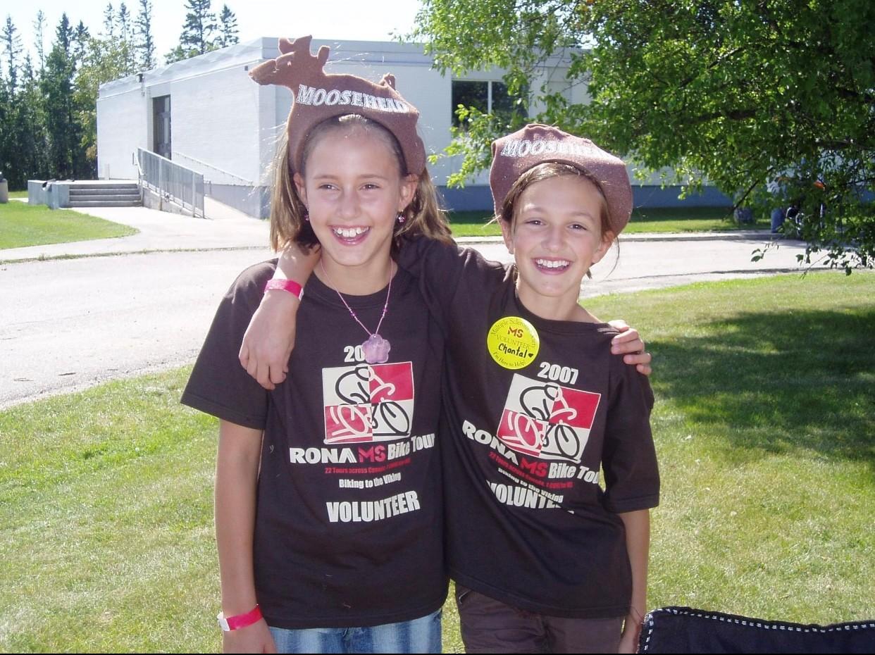Mika and her cousin as young girls smiling wearing matching black MS Bike volunteer t-shirts.