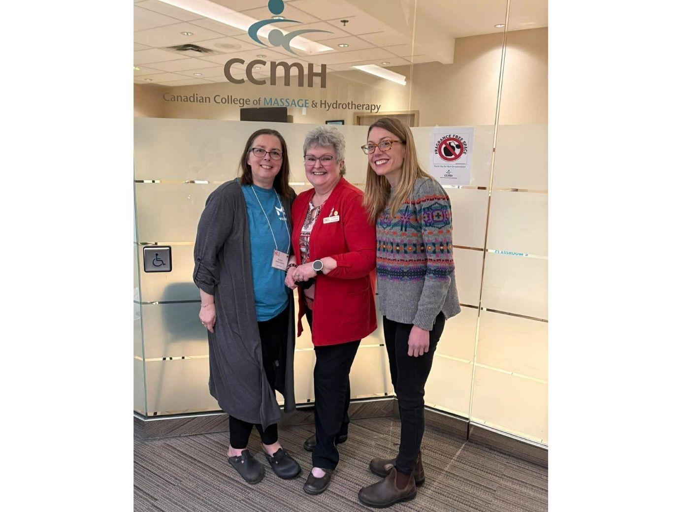 Three women smiling together in front of a CCMH office entrance sign.