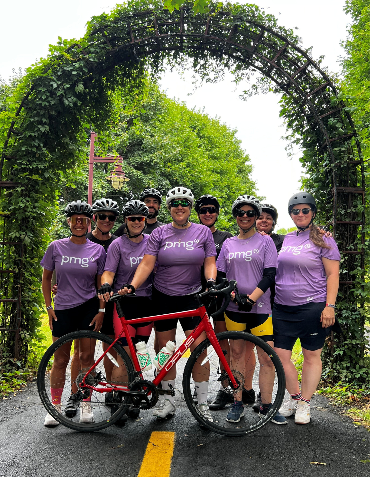 Chantal and the PMG team in purple shirts posing under a lush green vine archway on a road.