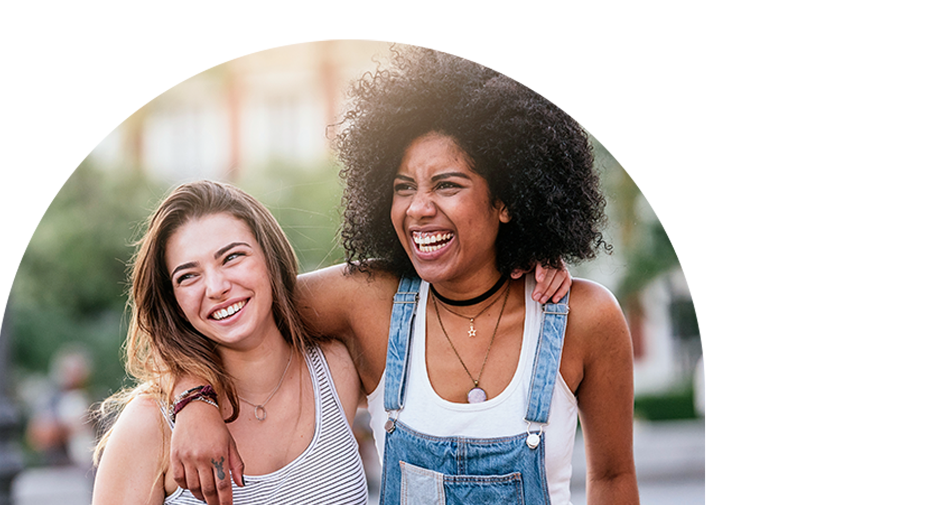 Two young women smiling and laughing together outdoors on a sunny day.