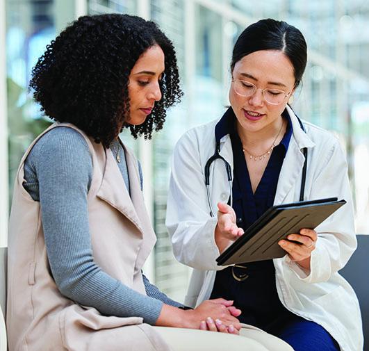 Doctor in white coat showing tablet screen to a patient during consultation.