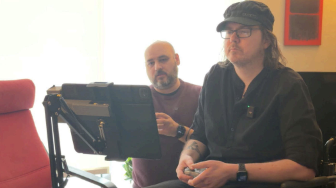 Jason and Edward sitting in a room, Jason is using the adaptive camera tablet while Edward sits beside him. 