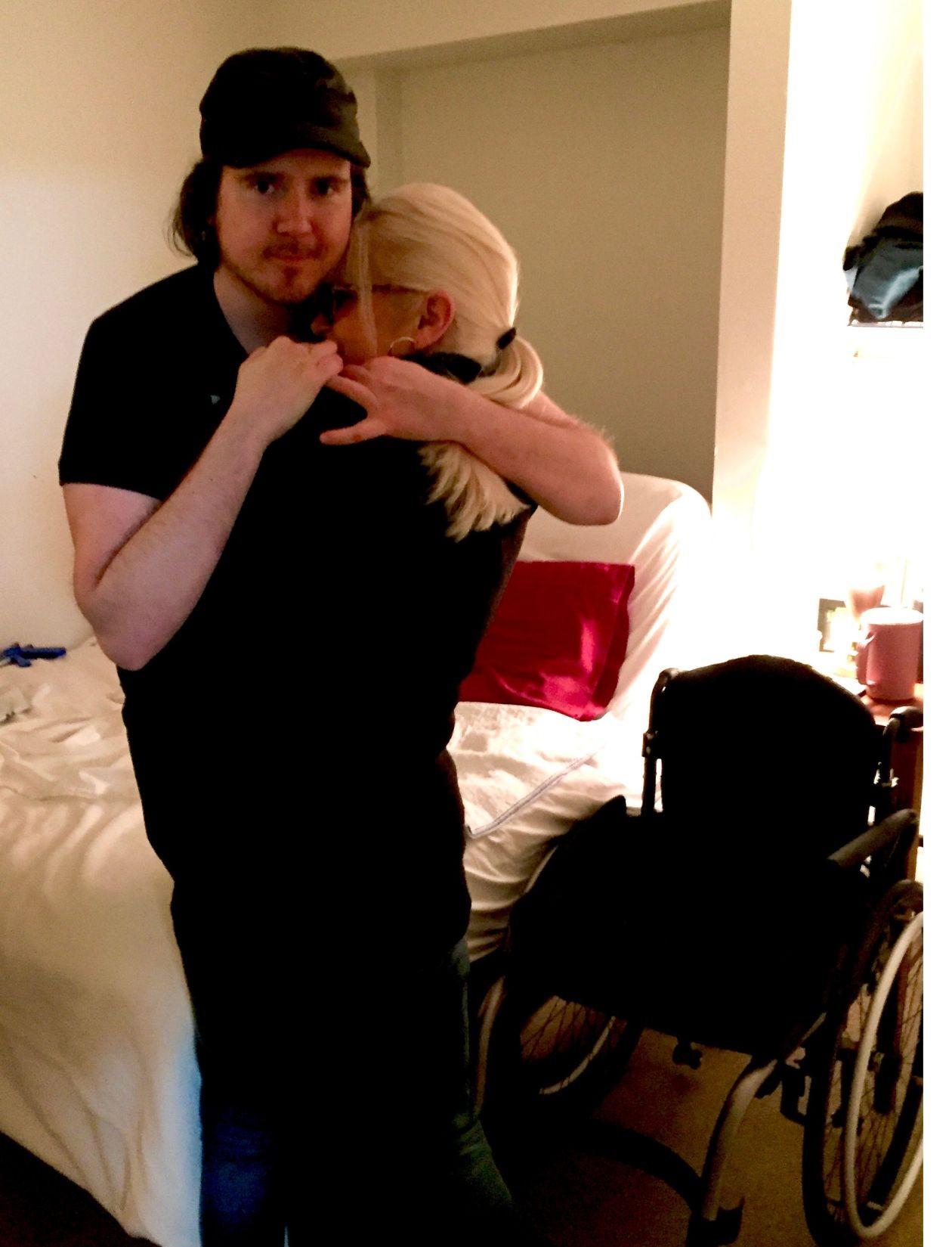 Jason and his mom hugging in a bedroom, with a wheelchair visible nearby.