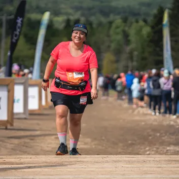 Andrea, wearing a red t-shirt and black shorts crosses the finish line and smiles proudly.