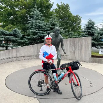 Marcel standing with his bike in front of a Terry Fox monument in St. John's, Newfoundland.