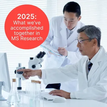 Two researchers in white lab coats. One wearing glasses and pointing at a computer screen and one holding a clipboard and pen.