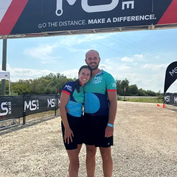 Mika and her husband smiling under the MS Bike event banner.
