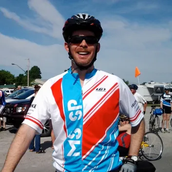 Craig wearing an MS Bike jersey standing in front of his bike outside.