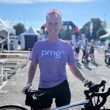 Chantal standing with a road bike at an outdoor event, wearing a purple PMG shirt.