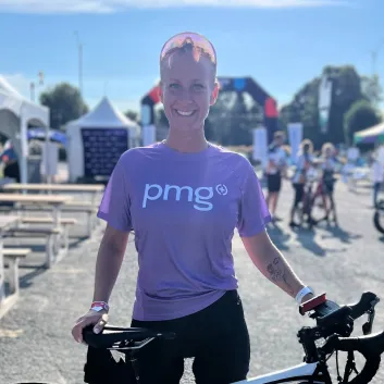 Chantal standing with a road bike at an outdoor event, wearing a purple PMG shirt.