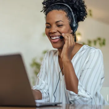 Smiling woman wearing a white blouse and headphones during a video call on her laptop.